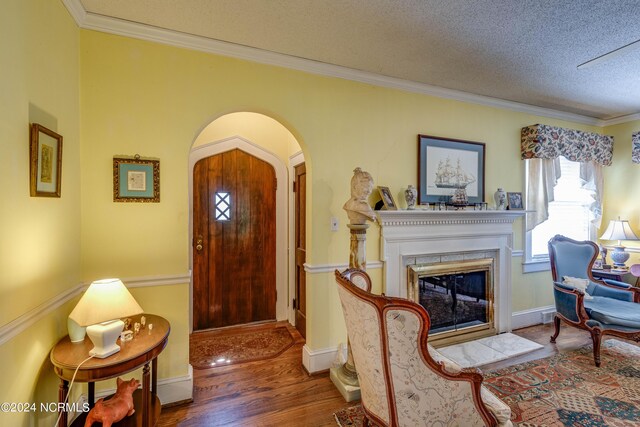 foyer entrance featuring arched walkways, a textured ceiling, a fireplace with flush hearth, wood finished floors, and ornamental molding