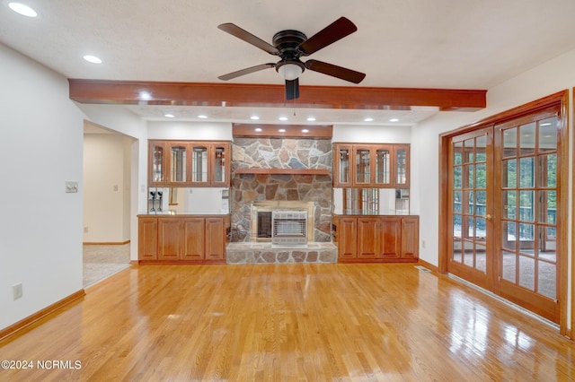 unfurnished living room with ceiling fan, light hardwood / wood-style flooring, french doors, beam ceiling, and a fireplace