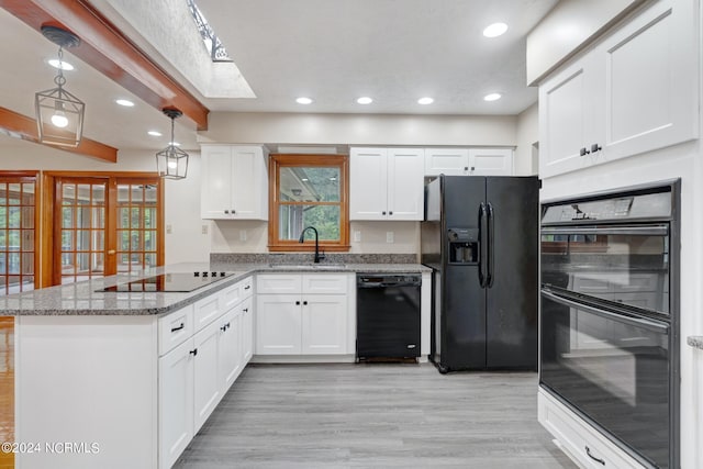 kitchen with decorative light fixtures, black appliances, light wood-type flooring, white cabinets, and a skylight