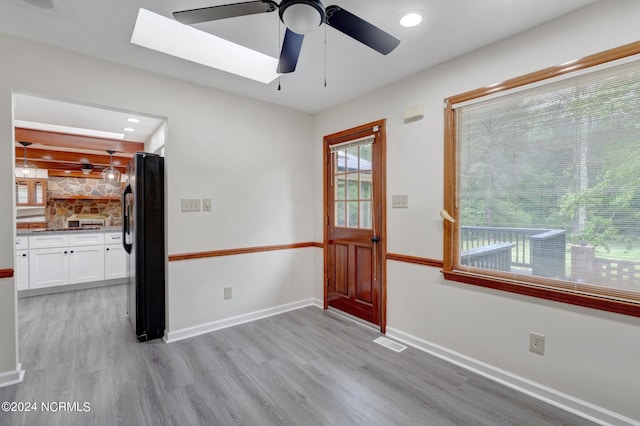 empty room with a skylight, ceiling fan, and light wood-type flooring