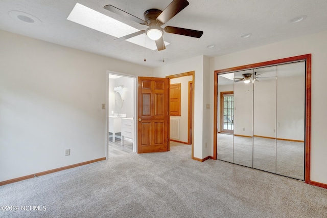 unfurnished bedroom featuring ceiling fan, a closet, ensuite bath, light colored carpet, and a skylight