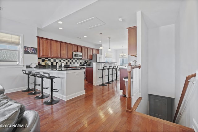 kitchen with backsplash, kitchen peninsula, decorative light fixtures, a breakfast bar area, and appliances with stainless steel finishes