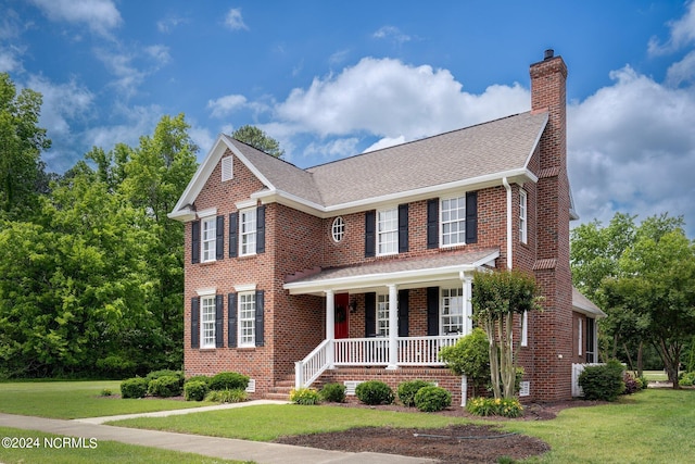 view of front of property featuring a porch, a chimney, a front lawn, and brick siding