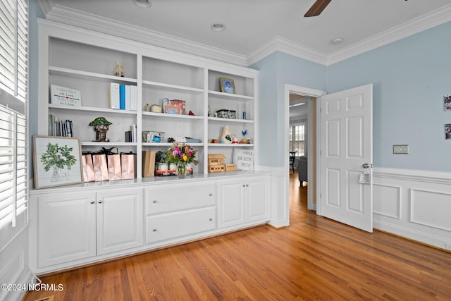 unfurnished room featuring ceiling fan, light wood-style flooring, a wainscoted wall, built in features, and crown molding