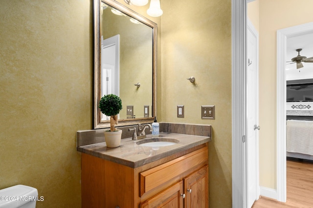 half bath with toilet, a ceiling fan, wood finished floors, and vanity