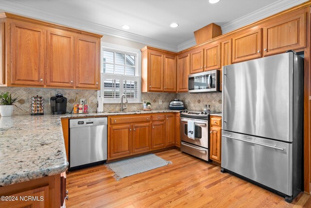 kitchen with appliances with stainless steel finishes, brown cabinets, light stone counters, ornamental molding, and a sink