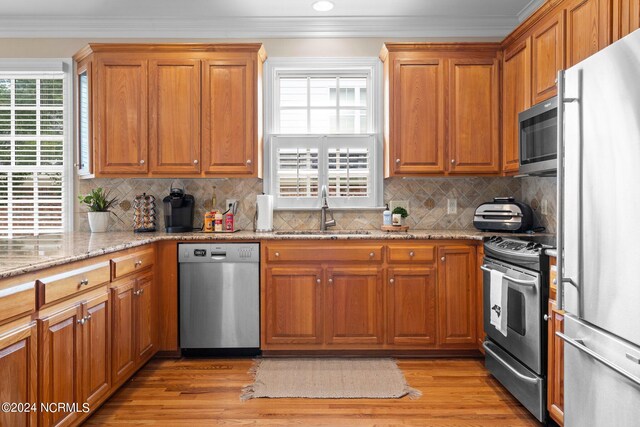 kitchen with stainless steel appliances, crown molding, a sink, and light stone counters