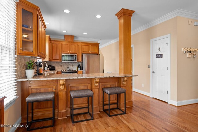 kitchen with stainless steel appliances, glass insert cabinets, brown cabinetry, ornamental molding, and a peninsula