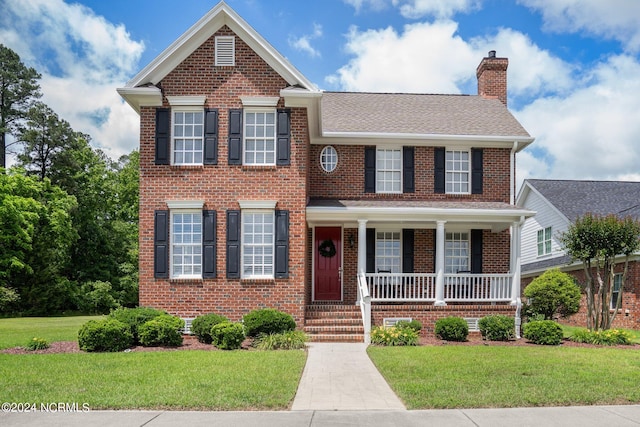 traditional-style house featuring covered porch, brick siding, a chimney, and a front lawn