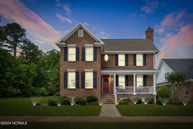 traditional home featuring covered porch, brick siding, a chimney, and a front yard