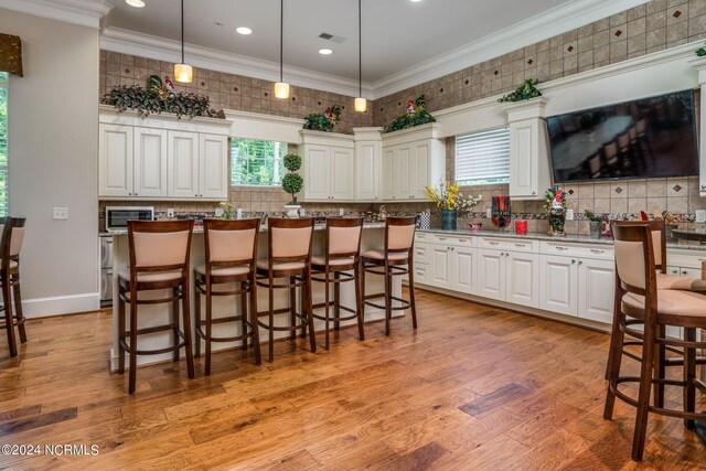 kitchen featuring ornamental molding, light wood-type flooring, a kitchen island, and decorative light fixtures