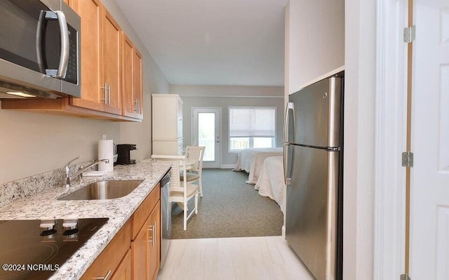 kitchen with sink, light stone counters, light carpet, and appliances with stainless steel finishes