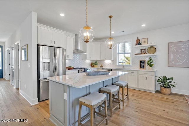 kitchen with stainless steel appliances, sink, white cabinetry, a kitchen island, and wall chimney range hood