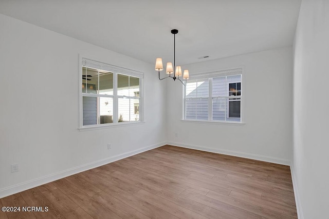 empty room with light hardwood / wood-style floors and a chandelier