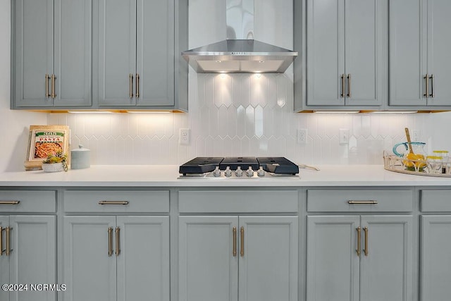 kitchen featuring stainless steel gas cooktop, wall chimney range hood, gray cabinets, and tasteful backsplash