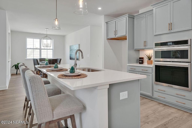 kitchen featuring sink, a center island with sink, stainless steel double oven, and gray cabinetry