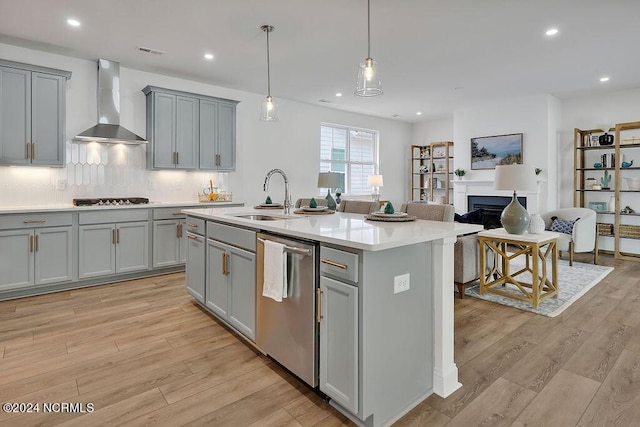 kitchen with sink, dishwasher, a center island with sink, and wall chimney exhaust hood