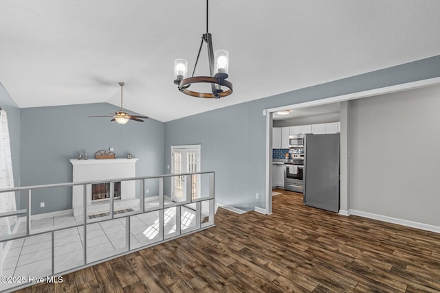 interior space featuring vaulted ceiling, ceiling fan with notable chandelier, a fireplace, and dark hardwood / wood-style flooring