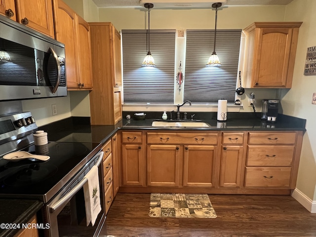 kitchen featuring dark wood-type flooring, a sink, appliances with stainless steel finishes, dark countertops, and decorative light fixtures