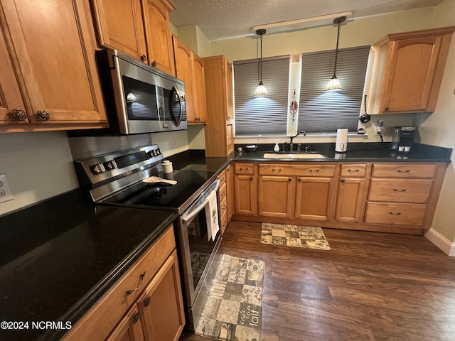 kitchen featuring dark countertops, appliances with stainless steel finishes, brown cabinets, decorative light fixtures, and a sink