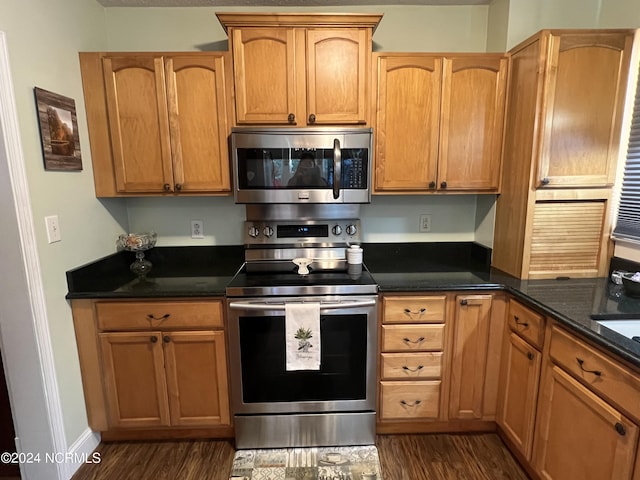 kitchen with dark stone counters, stainless steel appliances, dark wood-style flooring, and brown cabinetry