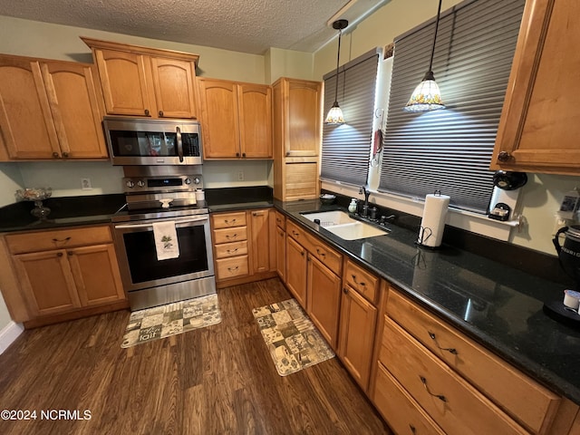 kitchen with dark wood-style flooring, hanging light fixtures, appliances with stainless steel finishes, a sink, and a textured ceiling