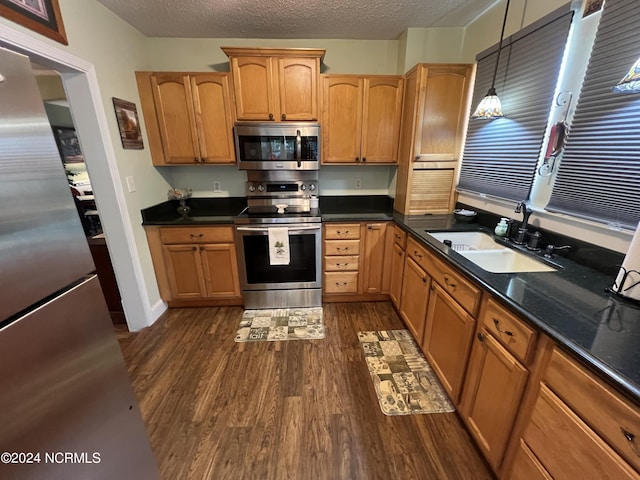 kitchen featuring a textured ceiling, a sink, appliances with stainless steel finishes, dark wood finished floors, and decorative light fixtures