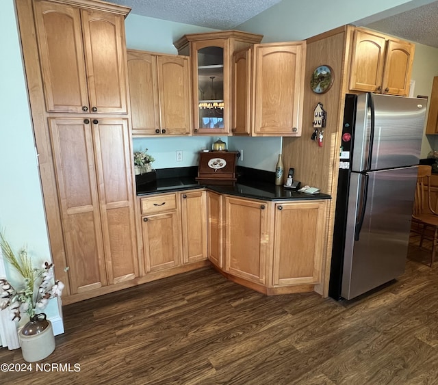 kitchen with dark countertops, glass insert cabinets, freestanding refrigerator, dark wood-type flooring, and a textured ceiling