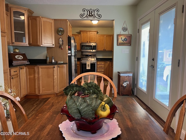 kitchen with dark wood-style floors, french doors, stainless steel appliances, dark countertops, and glass insert cabinets