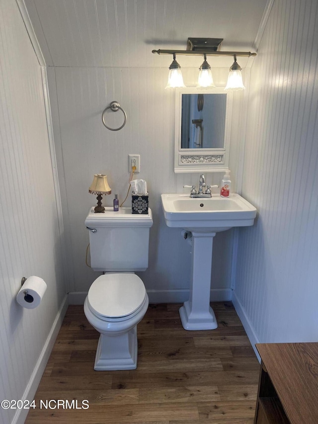 half bath with baseboards, toilet, and wood finished floors