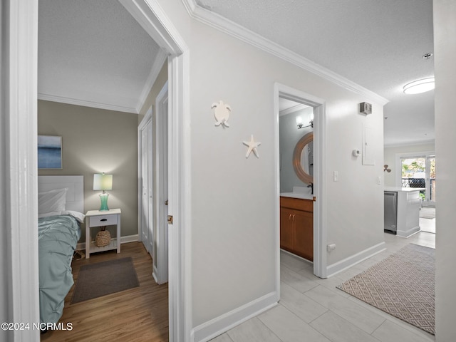 hallway with ornamental molding, light hardwood / wood-style flooring, and a textured ceiling