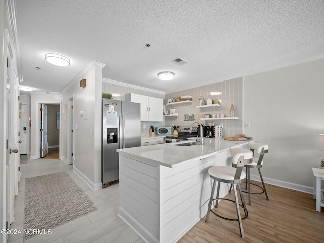 kitchen with stainless steel refrigerator with ice dispenser, kitchen peninsula, crown molding, white cabinetry, and a breakfast bar