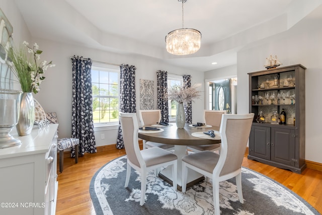 dining space featuring a raised ceiling, an inviting chandelier, and light wood-type flooring