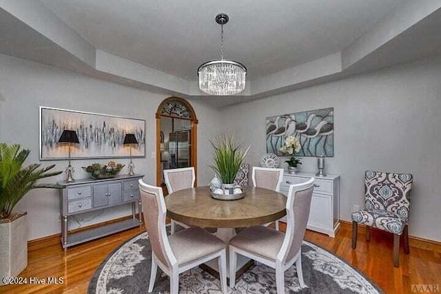 dining space featuring a raised ceiling, wood-type flooring, and a chandelier