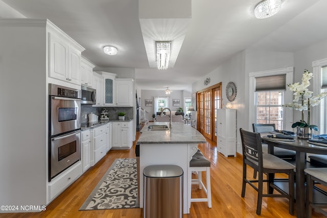 kitchen with stainless steel appliances, sink, light hardwood / wood-style flooring, white cabinetry, and an island with sink