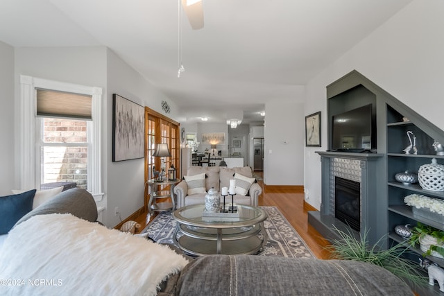 living room featuring wood-type flooring, ceiling fan, and a tiled fireplace