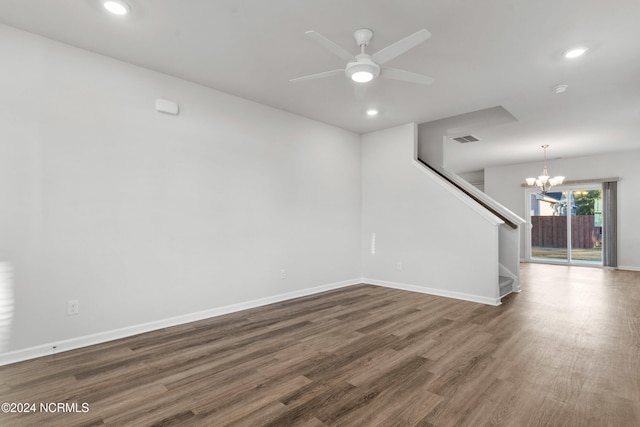 empty room with ceiling fan with notable chandelier, wood finished floors, visible vents, baseboards, and stairs