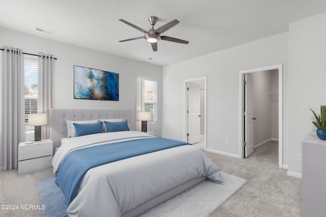 bedroom featuring ceiling fan, light carpet, visible vents, baseboards, and a walk in closet