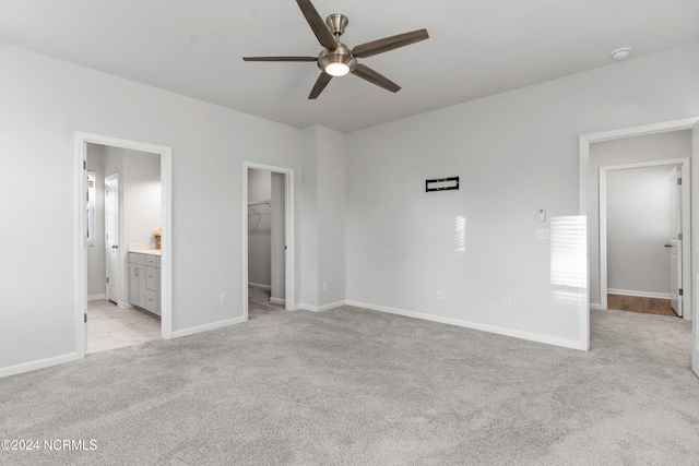 unfurnished bedroom with ensuite bathroom, light carpet, baseboards, a closet, and a walk in closet