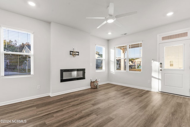 unfurnished living room with a glass covered fireplace, visible vents, baseboards, and wood finished floors