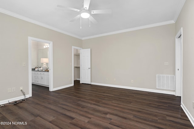 unfurnished bedroom with a walk in closet, connected bathroom, ceiling fan, dark wood-type flooring, and ornamental molding