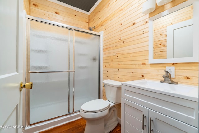 bathroom with wood-type flooring, a shower with shower door, wooden walls, toilet, and vanity