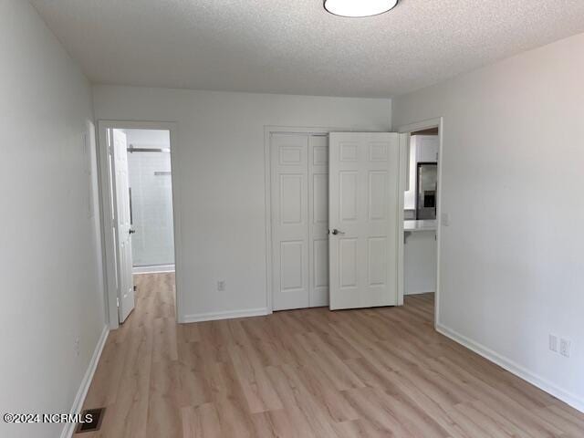 unfurnished bedroom with a closet, light hardwood / wood-style floors, a textured ceiling, and ensuite bathroom