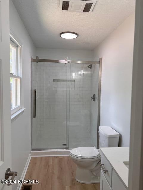 bathroom featuring toilet, hardwood / wood-style flooring, a shower with door, vanity, and a textured ceiling