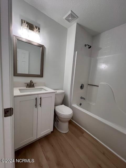 full bathroom featuring wood-type flooring, washtub / shower combination, a textured ceiling, toilet, and vanity