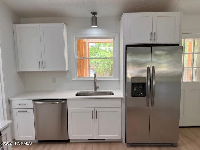 kitchen with appliances with stainless steel finishes, light hardwood / wood-style floors, white cabinets, and a wealth of natural light