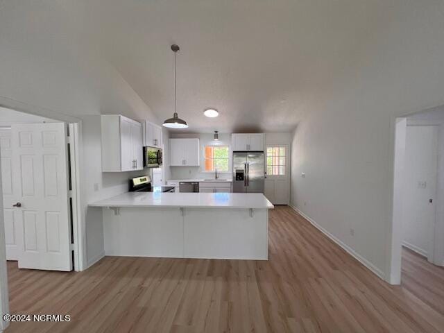 kitchen featuring hanging light fixtures, appliances with stainless steel finishes, white cabinetry, and light hardwood / wood-style flooring