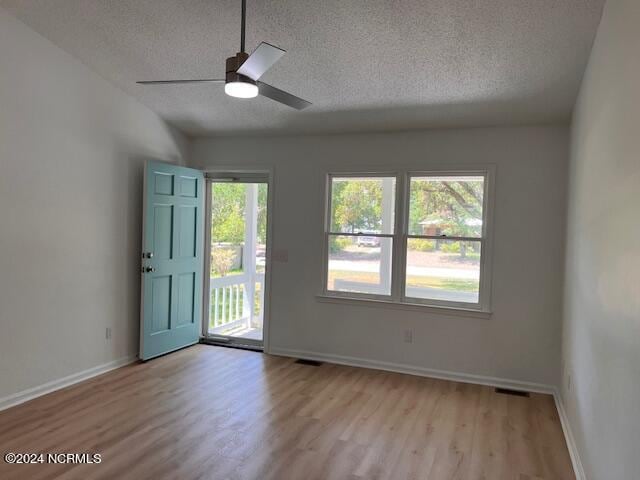 empty room with a wealth of natural light, ceiling fan, light hardwood / wood-style floors, and a textured ceiling