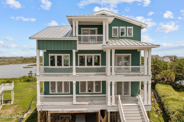 rear view of house with metal roof, a balcony, a water view, stairway, and a standing seam roof