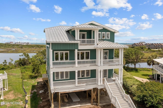 rear view of house featuring a standing seam roof, a water view, metal roof, and a balcony